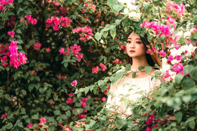 Portrait of beautiful young woman standing by pink flowering plants