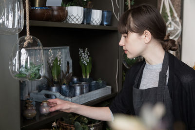 Young female entrepreneur arranging decorations on shelf at store