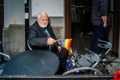 Smiling man holding camera while sitting outdoors