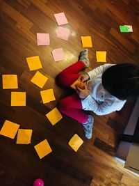 Directly above shot of girl sitting by adhesive notes on hardwood floor