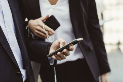 Midsection of business professional using smart phone while standing with female colleague outdoors