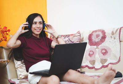 Young woman using phone while sitting on bed at home