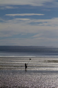 Silhouette man holding broom while standing at beach against sky