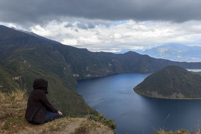 Rear view of man sitting on mountain against sky