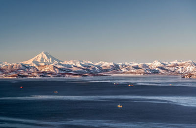 Scenic view of sea amidst snowcapped mountains against clear sky