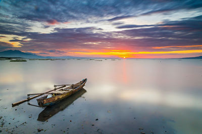 Boat moored on lake against sky during sunset