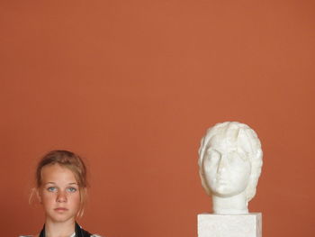 Portrait of girl standing by statue against brown background