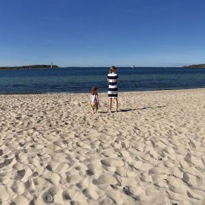 Rear view of mother and son standing on sand at beach