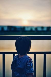 Rear view of boy standing against railing