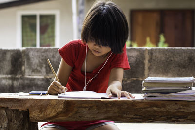 A girl sitting on a wooder table doing homework. home schooling. write online at home