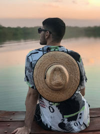Rear view of man looking at lake against sky during sunset