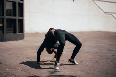 Woman bending over backwards in front of wall