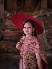 Portrait of woman holding umbrella while standing against red wall