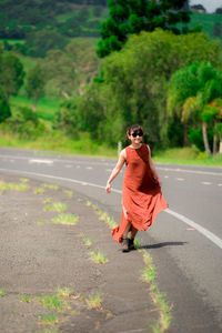 Young woman wearing sunglasses walking on road against trees in forest