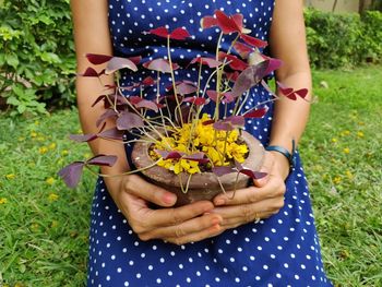 Midsection of woman holding flowering plant in field