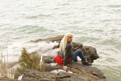 High angle view of transgender male sitting on rocks by sea