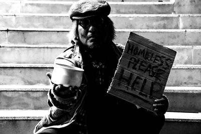 Close-up of beggar with message and bowl sitting on steps