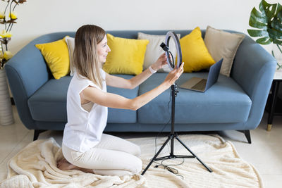 Young woman making photo or video content for social media with smartphone and light of ring lamp.