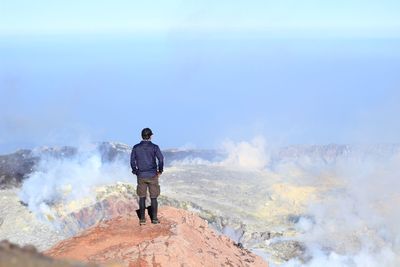 Rear view of man standing on mountain against sky