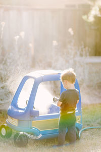 Toddler boy washing a toy car in the summer sun