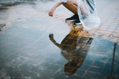 Low section of woman crouching by puddle