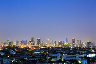 Illuminated buildings in city against clear sky at night