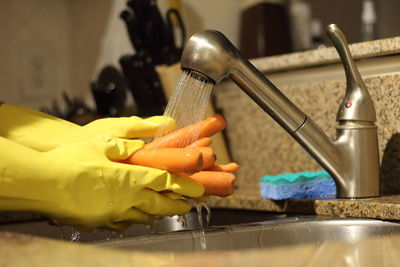 Cropped hands cleaning carrots in kitchen sink at home
