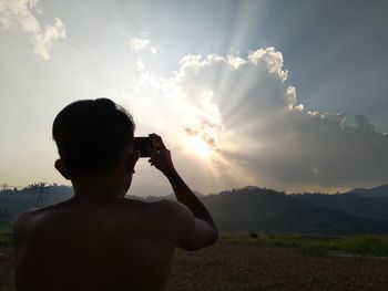 Rear view of man photographing against sky during sunset