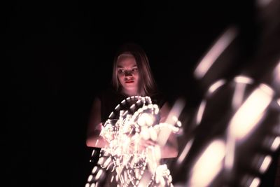 Thoughtful young woman holding illuminated string lights against black background