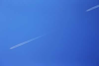 Low angle view of vapor trails against clear blue sky