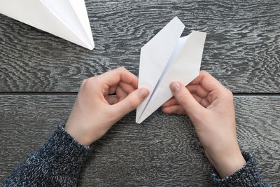 Cropped hands of woman making paper airplane on wooden table