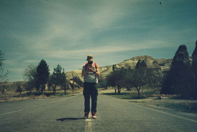 Rear view of man standing on road against sky