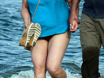 Midsection of couple holding hands while standing against sea