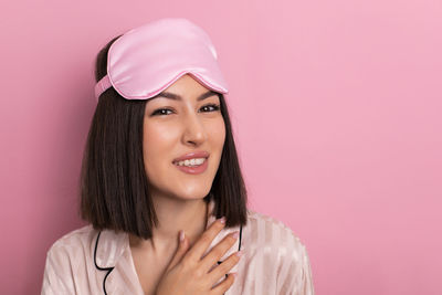 Portrait of young woman standing against pink background