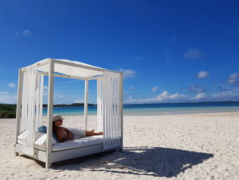 Full length of woman relaxing on four poster bed at beach during sunny day