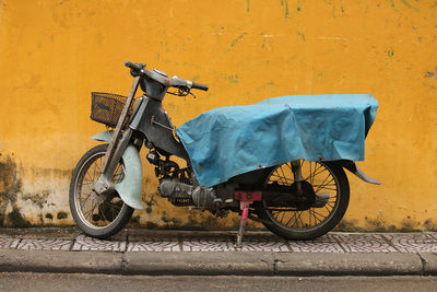 Parked bike covered with blue tarpaulin against yellow wall