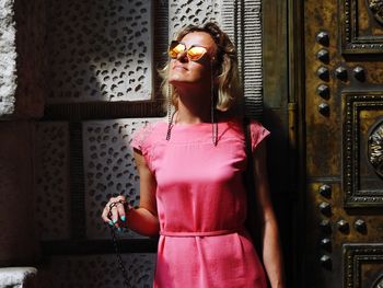 Young woman wearing sunglasses standing against pink wall