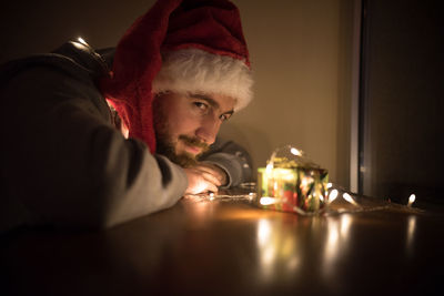 Close-up of young man by illuminated christmas lights on gift in darkroom