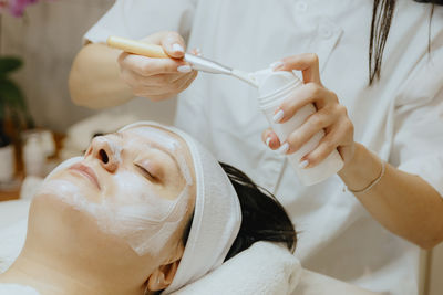 A girl cosmetologist squeezes a cream mask onto a brush for a woman s face.