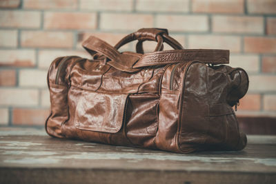 Close-up of leather bag on table against brick wall