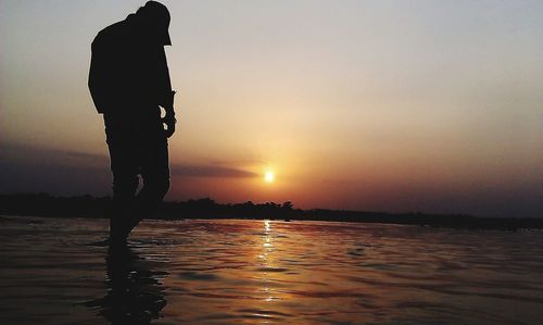 Silhouette man standing by sea against sky during sunset