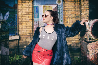 Young woman wearing sunglasses standing against built structure