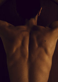 Rear view of shirtless man standing against black background