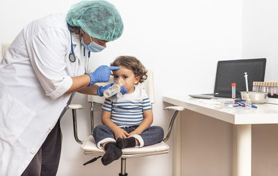 Paediatrician administers aerosolised medication while checking pneumonia in a blond caucasian boy.