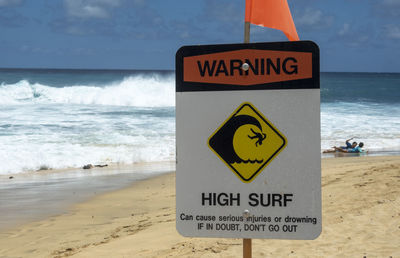 Warning sign on beach against sky