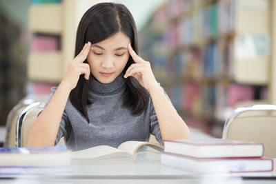 Young woman reading book while sitting at table in library