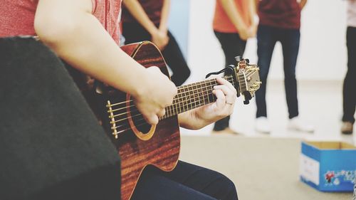 Midsection of woman playing guitar while sitting outdoors