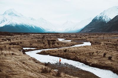 Scenic view of stream flowing amidst field by snowcapped mountain against sky