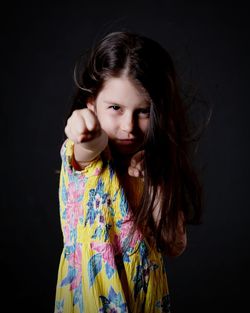 Portrait of girl gesturing while standing against black background