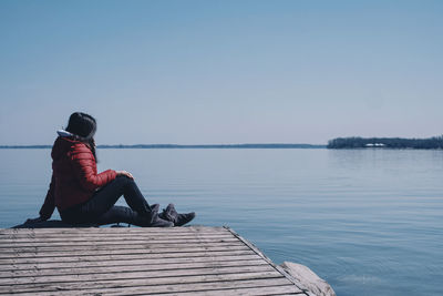 Man sitting on pier over lake against clear sky
